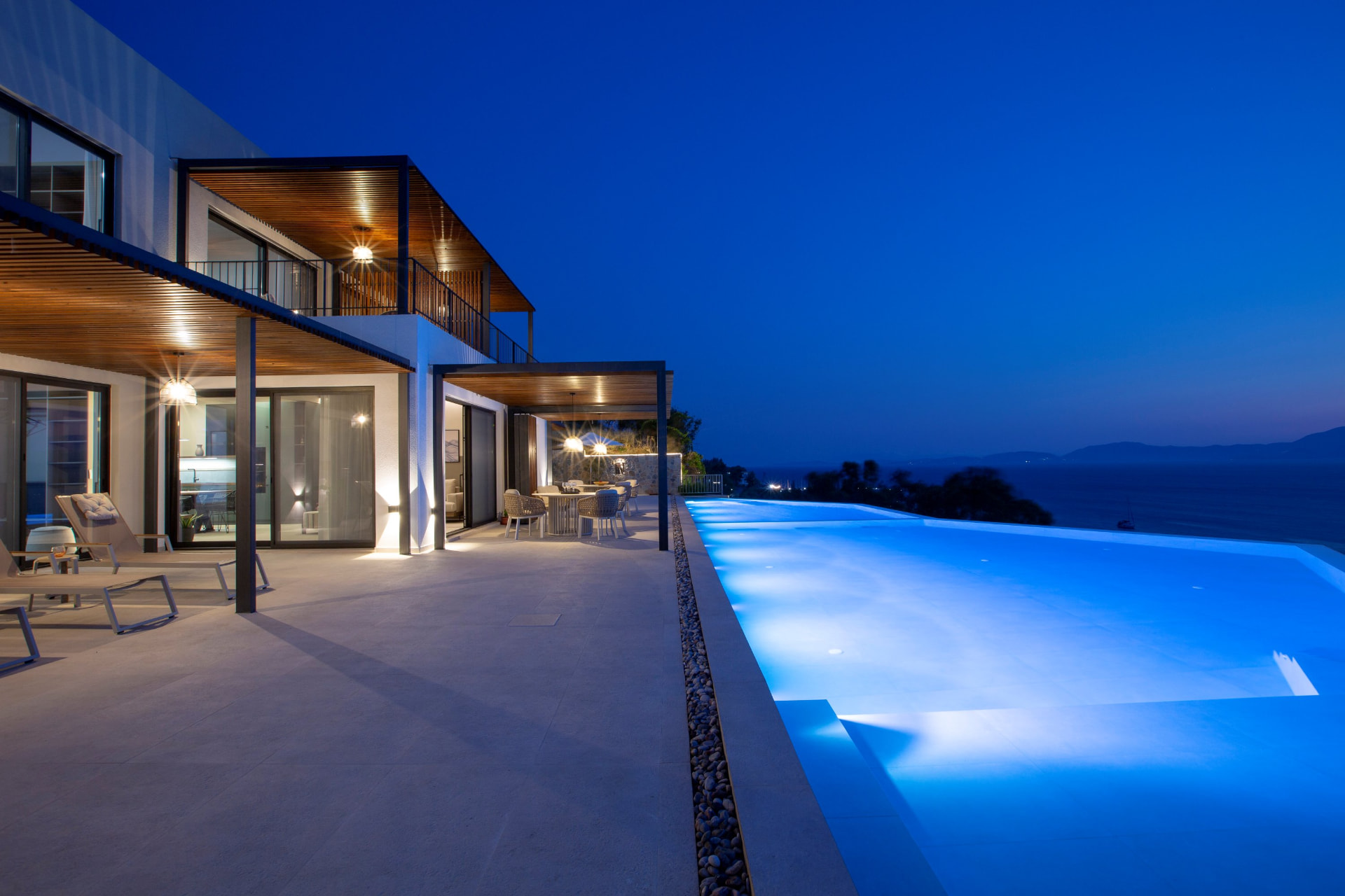 Illuminated pool and terrace at night with sea and distant lights
