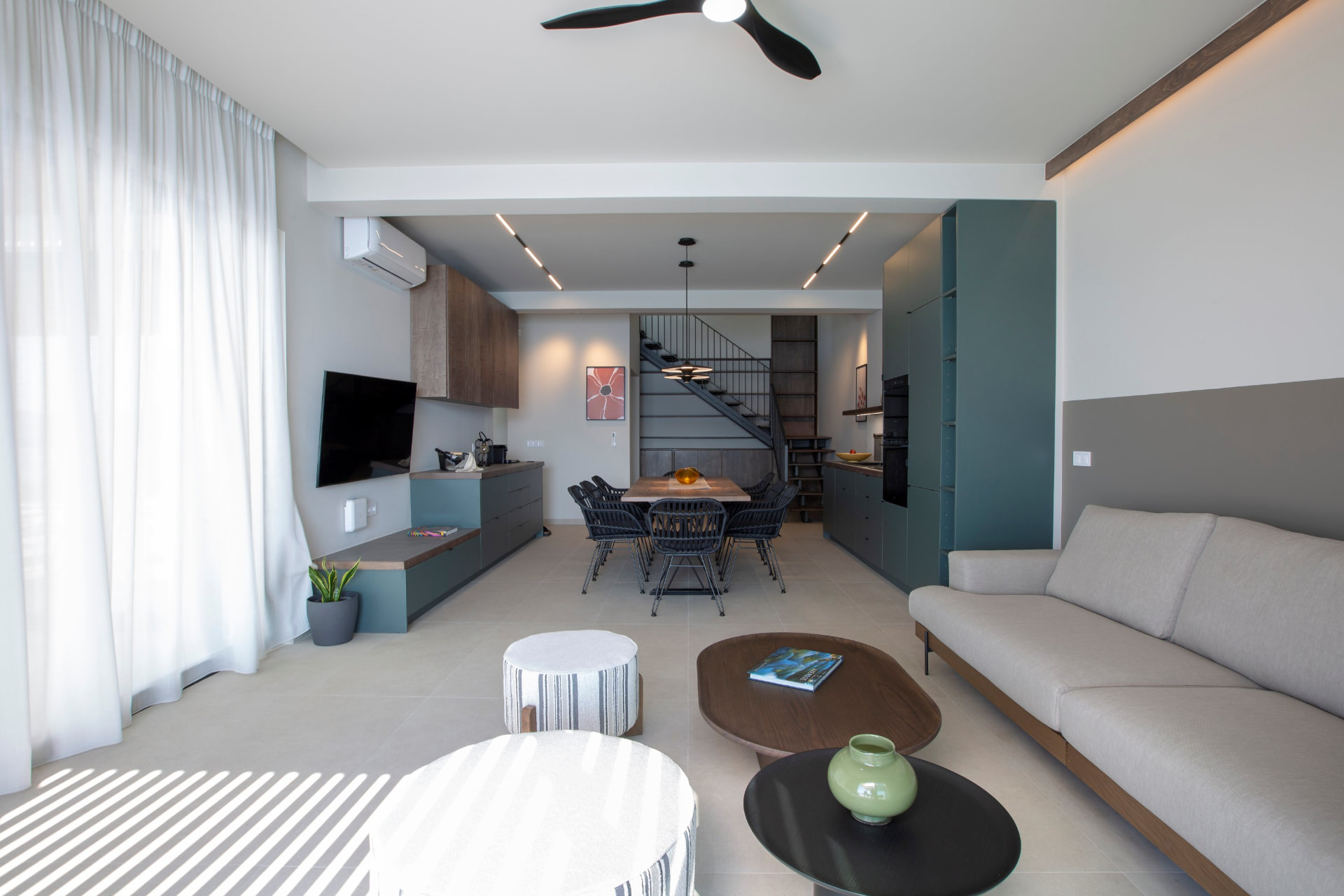 Open-plan living and dining area with teal kitchen and staircase