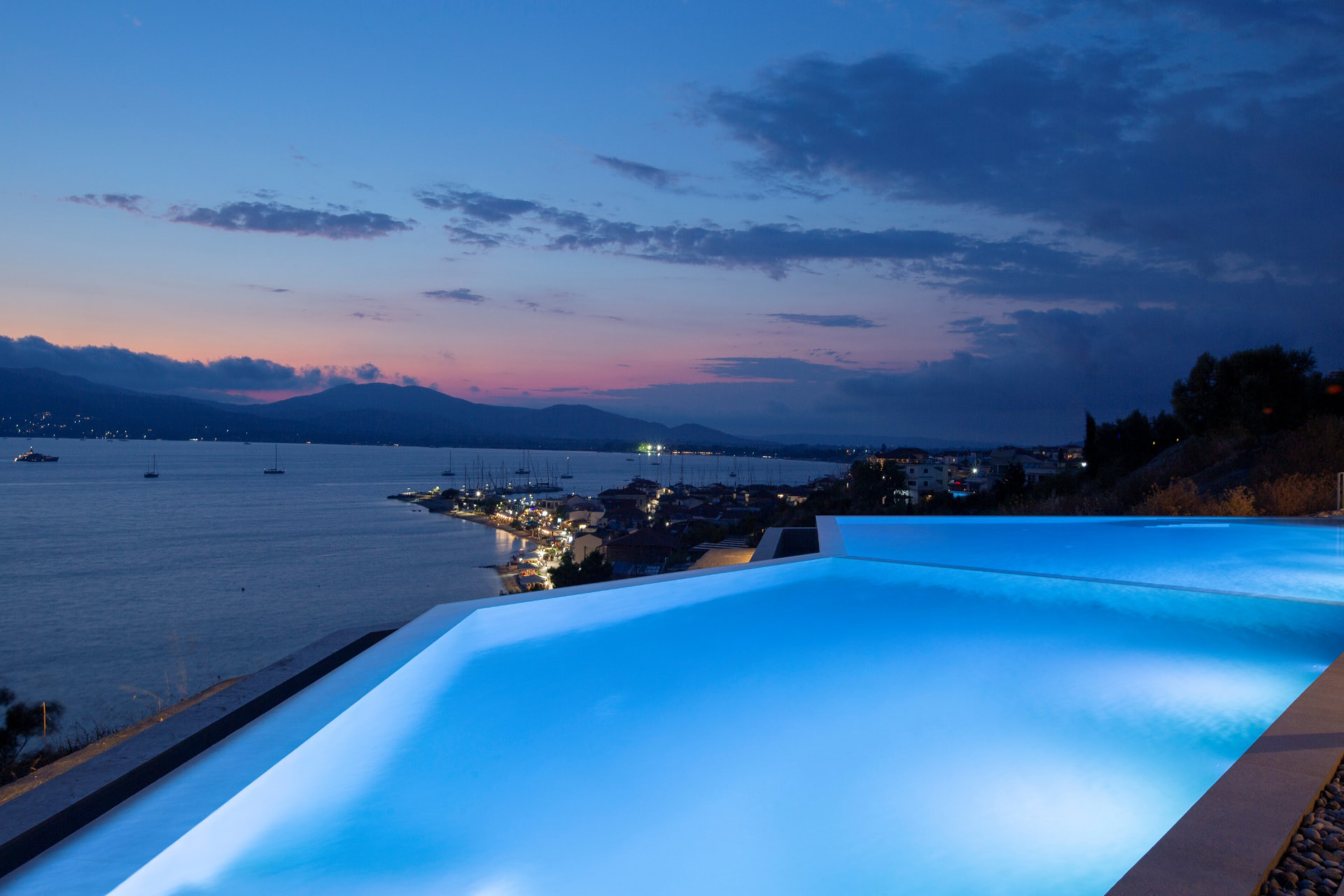 Lit infinity pool at twilight above Paleros harbour lights