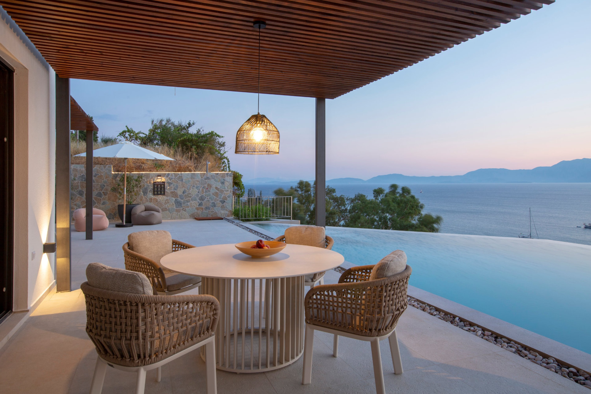 Round dining table under the pergola at dusk beside the infinity pool and sea