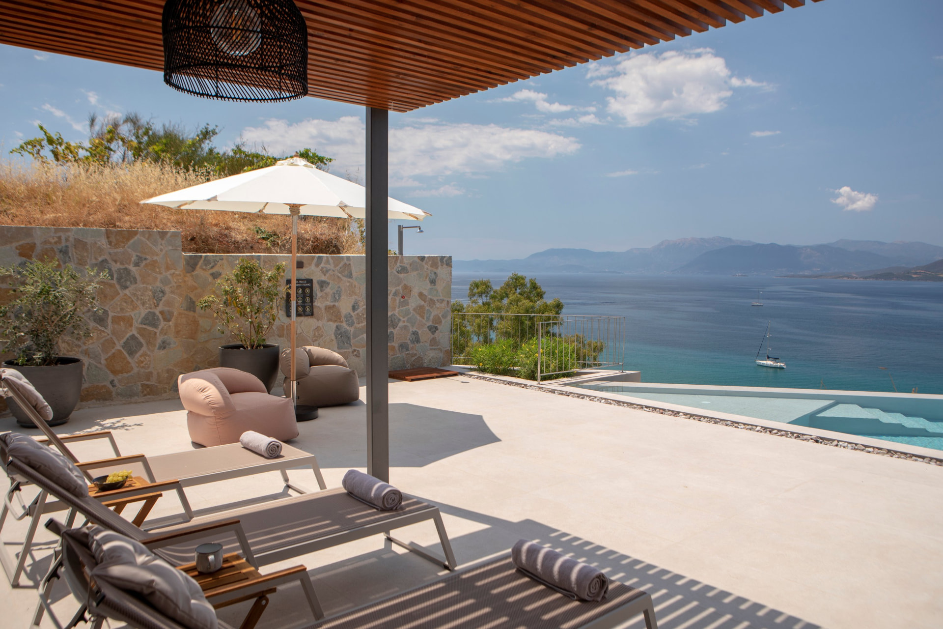 Sun loungers and shaded lounge chairs beside the infinity pool overlooking the sea