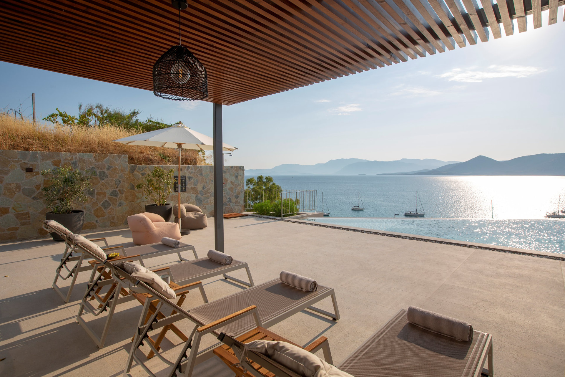 Shaded pergola terrace with sun loungers beside the infinity pool overlooking the Ionian Sea
