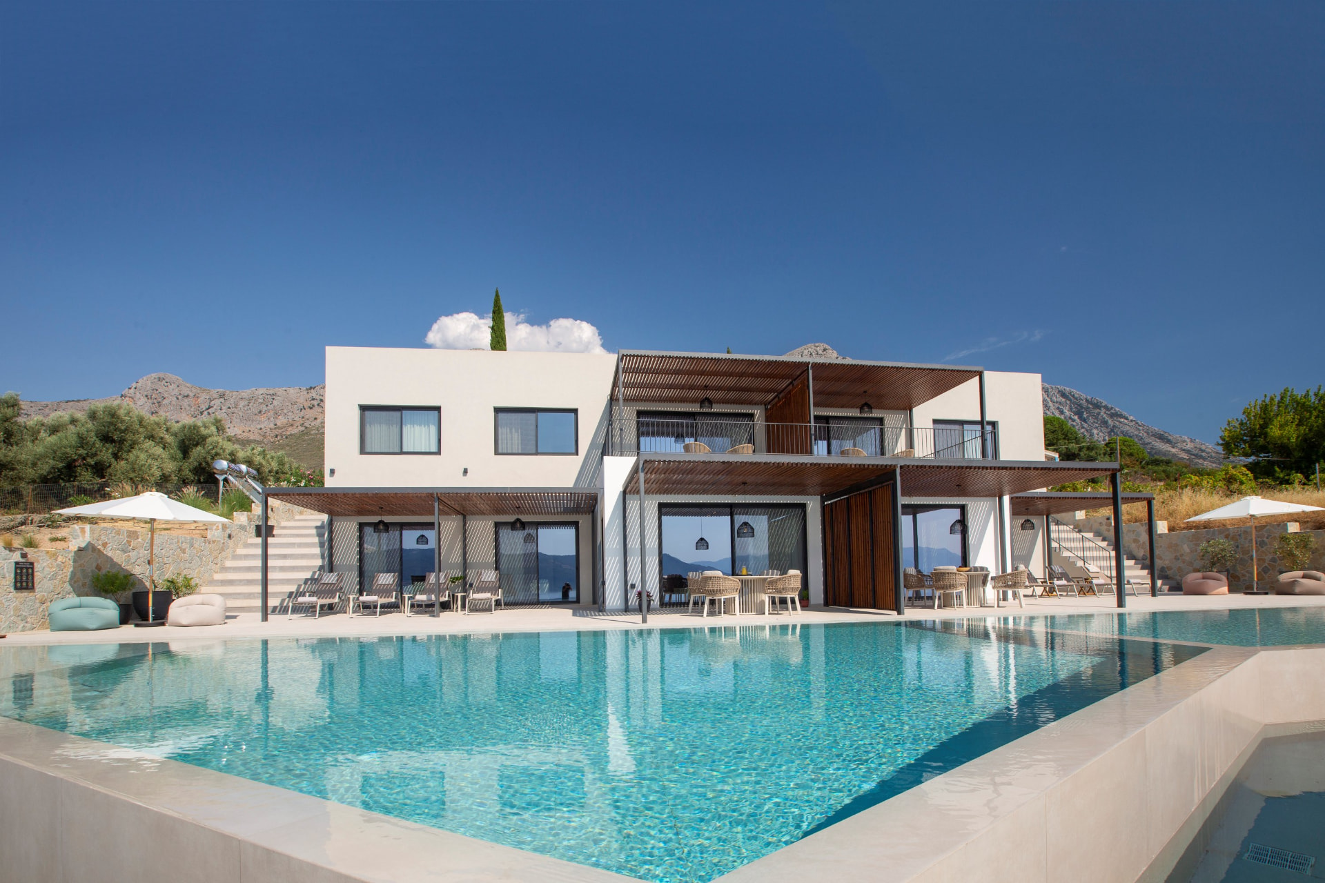 Full villa facade with large pool, shaded pergolas and mountain backdrop