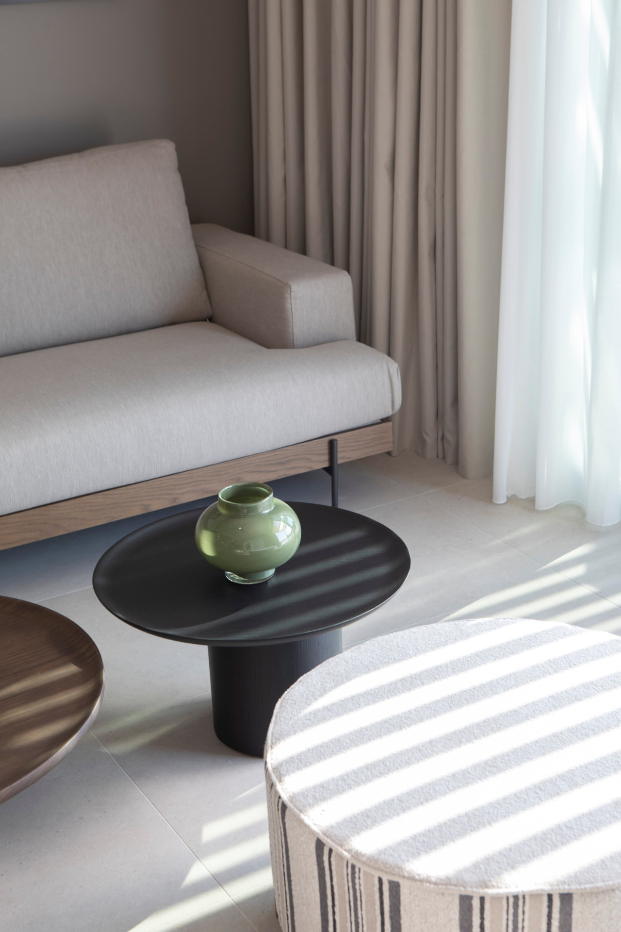 Living room detail with linen sofa, black side table and green glass vase in striped light