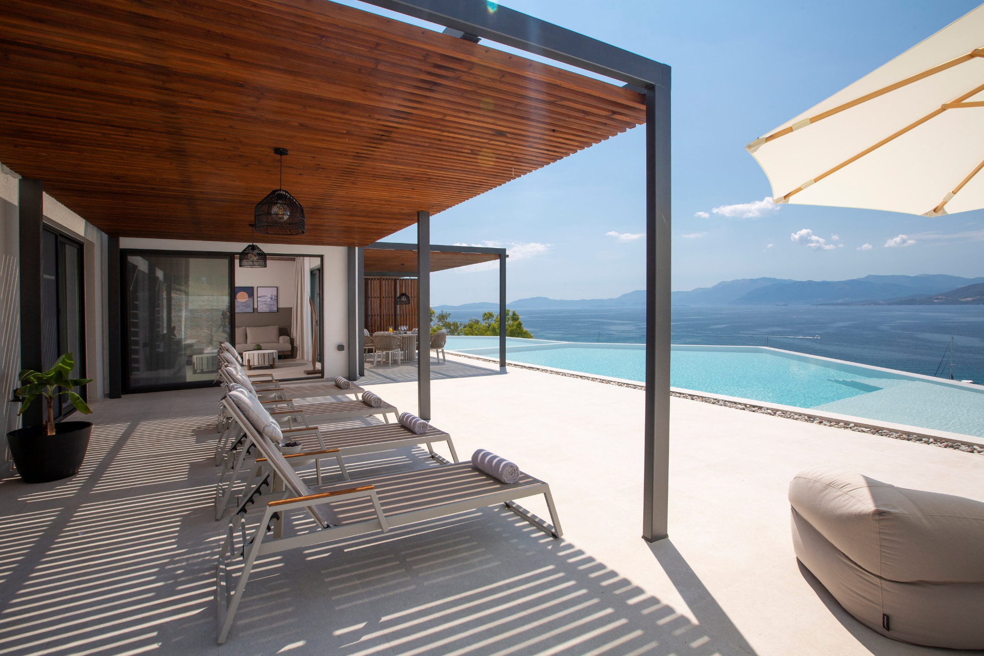 Shaded pergola terrace with sun loungers beside the infinity pool and open Ionian views