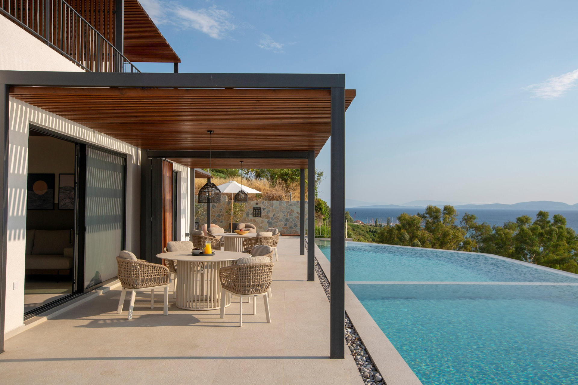 Poolside dining terrace with woven armchairs beside the infinity pool and sea beyond
