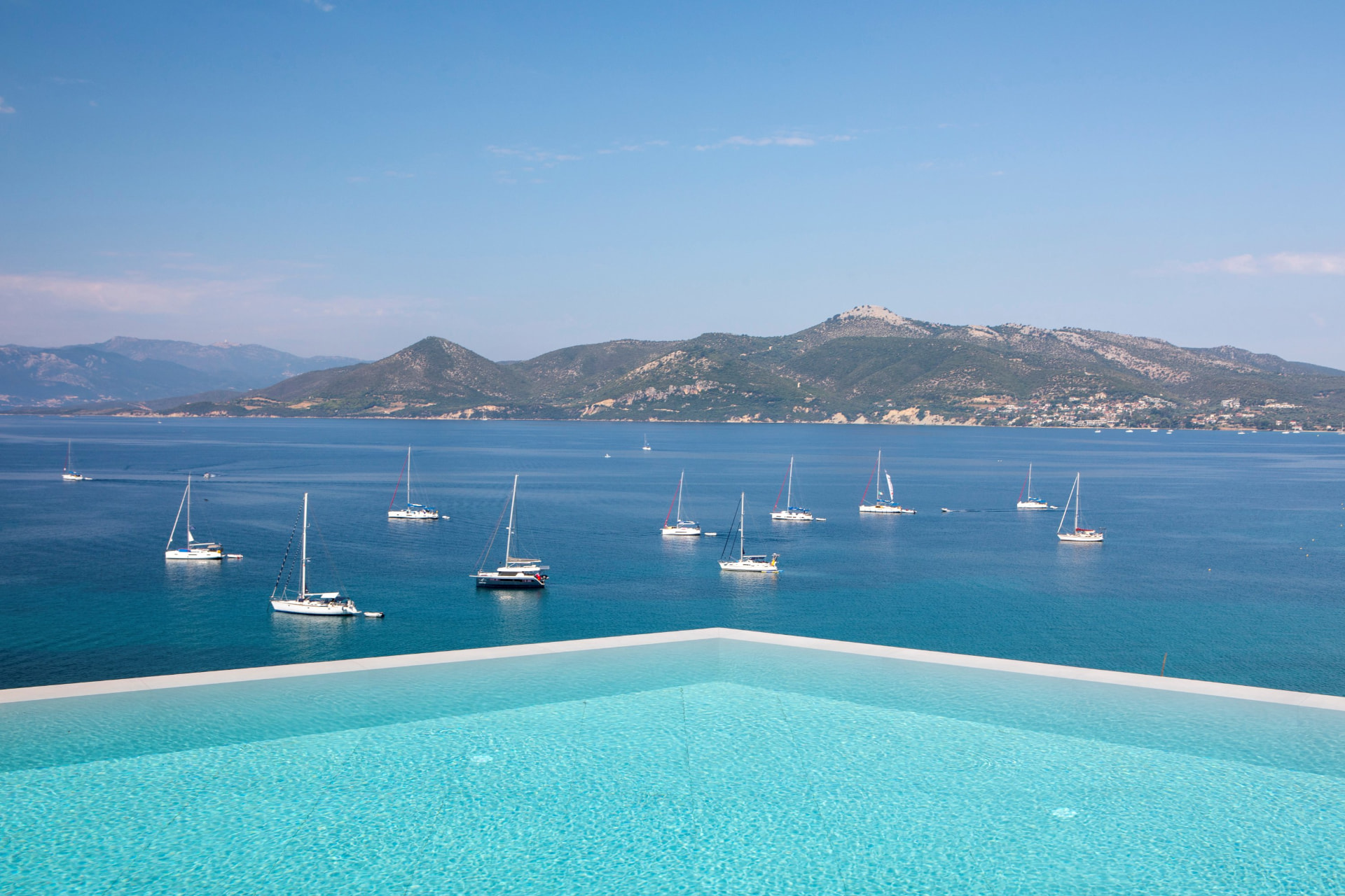 Infinity pool edge framing sailing boats anchored in the turquoise bay