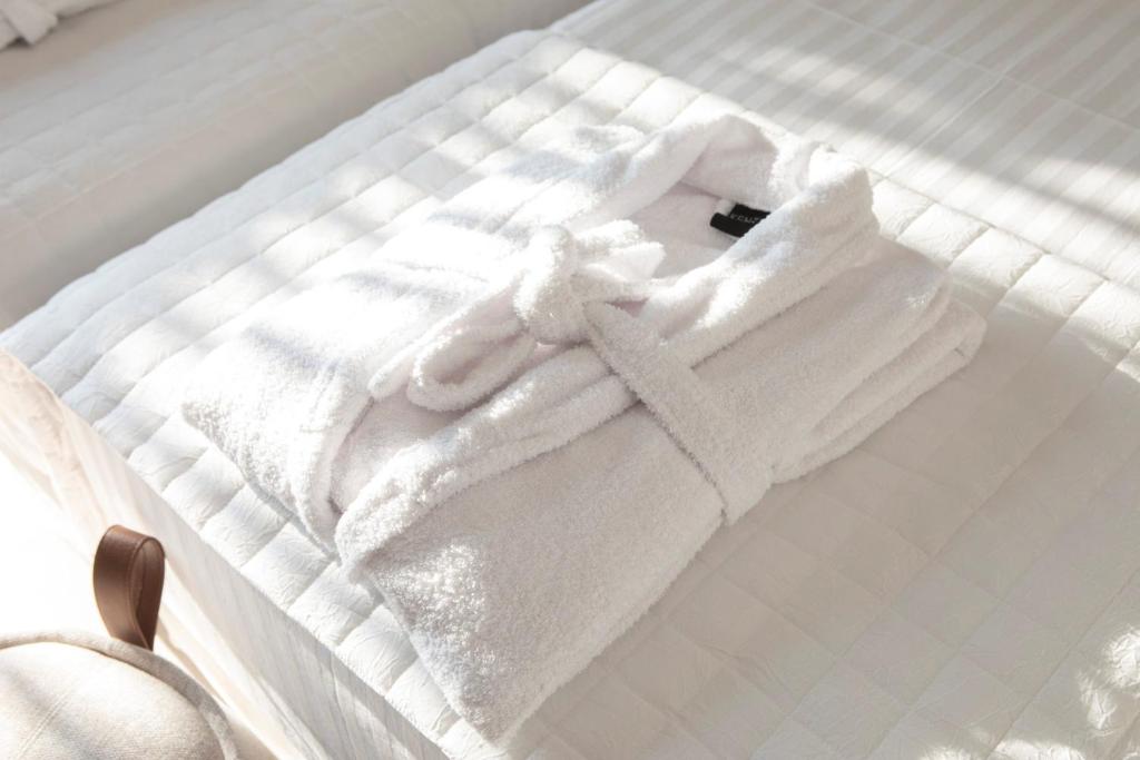 Folded bathrobes on a crisp white bed in morning sunlight