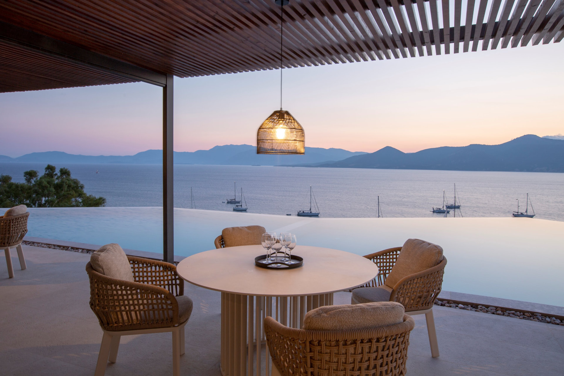 Round dining table for four under a pergola at sunset beside the infinity pool