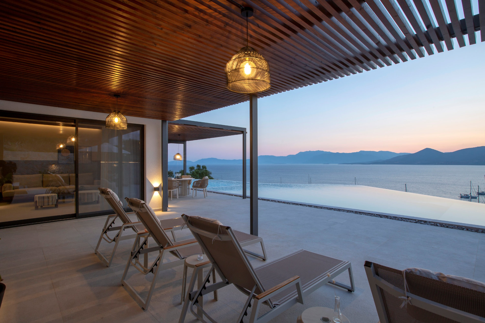 Poolside terrace at dusk with lantern lighting and infinity pool over the sea