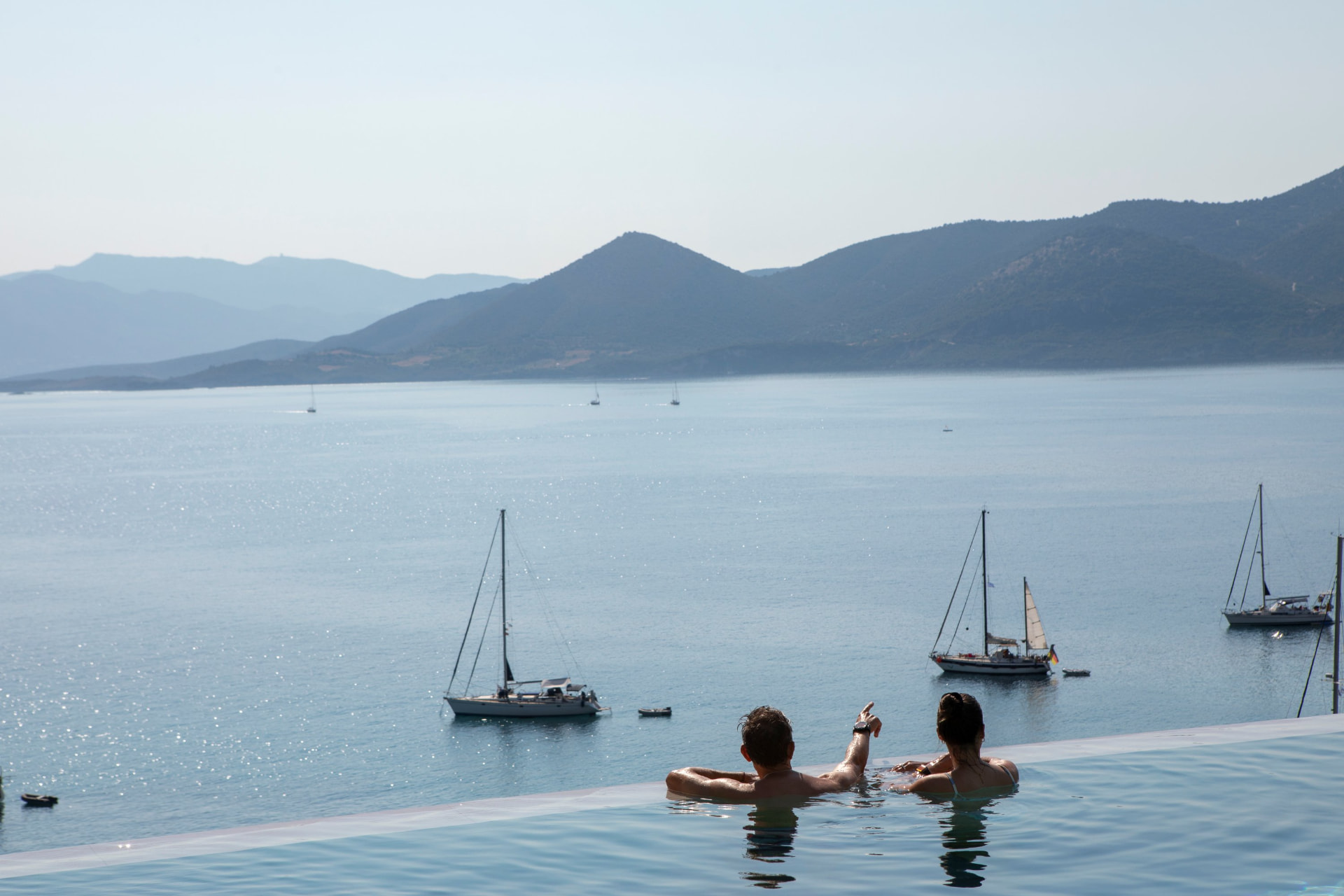 Couple relaxing in the infinity pool watching yachts in the bay